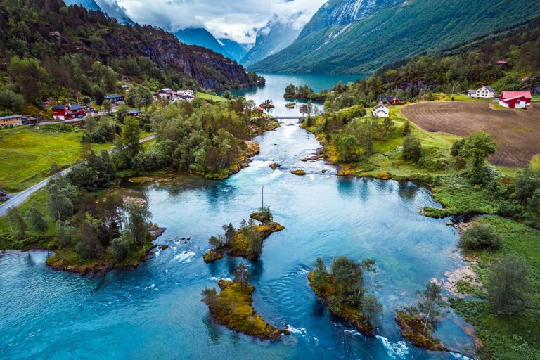 Aerial view of a scenic river splitting around small islands, surrounded by lush greenery, mountains, and scattered houses.