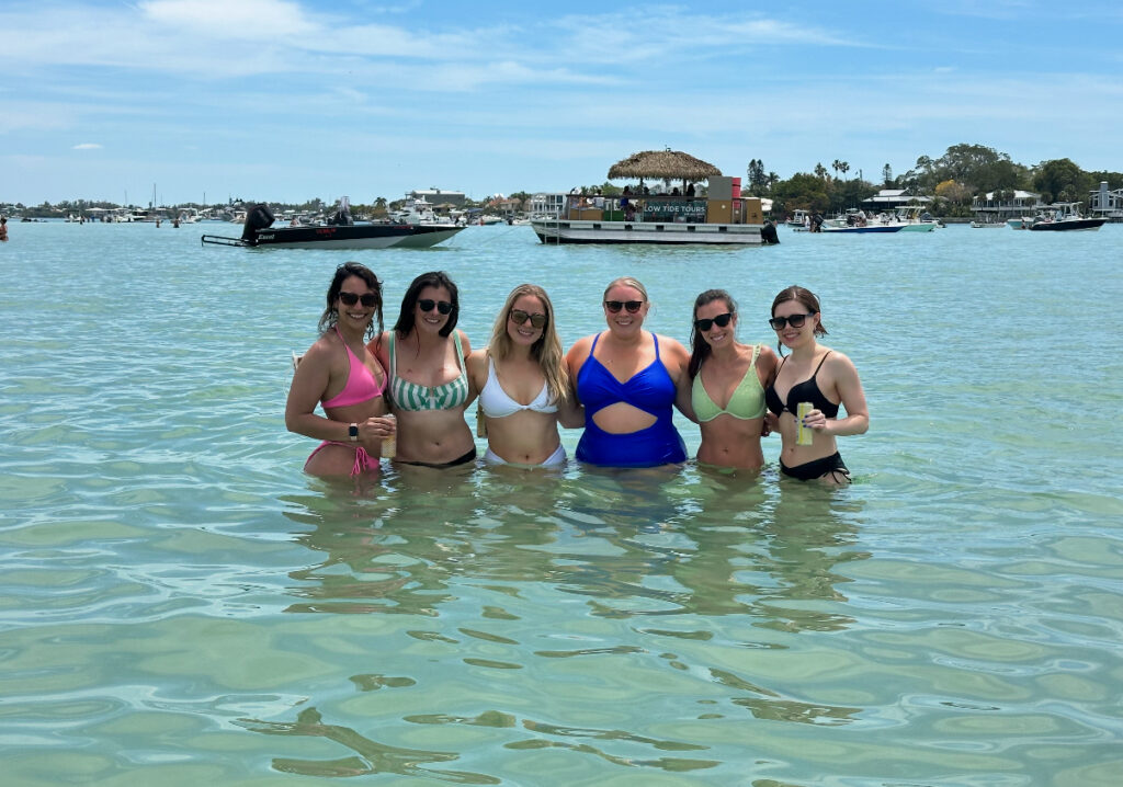 Six women in swimsuits stand together in shallow water
