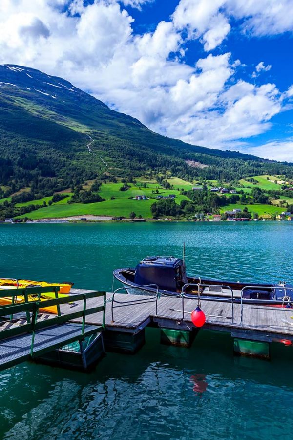 A scenic view of a dock on a tranquil lake, with small boats and vibrant green hills under a partly cloudy sky.